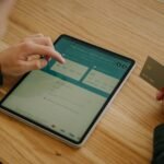 Person making an online payment using a tablet and credit card on a wooden desk.