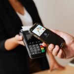 A person using a smartphone for contactless payment at a retail store counter.
